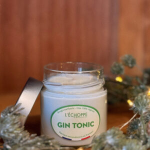 Bougie parfumée gin tonic dans un pot en verre avec couvercle métal posé à côté, contre un mur en bois.