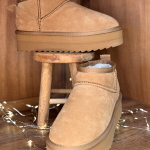 Boots fourrées femme camel en nubuck, tige basse style après-ski, semelle plateforme crantée ton sur ton, présentées sur tabouret en bois.