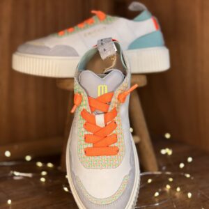 Basket femme blanche et grise à lacets orange fluo, empiècements menthe et turquoise, semelle épaisse blanche, posée sur étagère en bois avec deuxième chaussure au fond et guirlande lumineuse