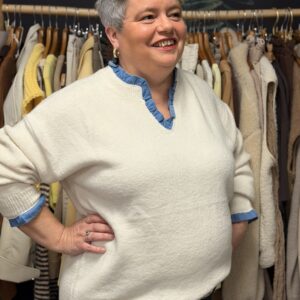Femme ronde portant pull écru col tunisien et chemise en jean bleu en dessous, look confortable dans une boutique de vêtements