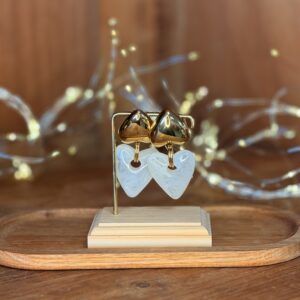 Boucles d’oreilles dorées avec pendentifs cœurs effet nacré exposées sur présentoir en bois