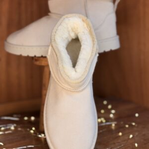 Boots femme blanches en mouton synthétique, tige courte, semelle crantée blanche, posées sur tabouret en bois avec guirlande lumineuse décorative