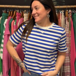 Jeune femme brune aux cheveux longs pose en souriant les mains sur les hanches, portant un t-shirt marinière bleu électrique et blanc. Vue de face