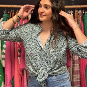 Jeune femme brune aux cheveux longs pose souriante, portant chemise fluide vert d’eau à motif floral nouée devant. Style frais printanier bohème