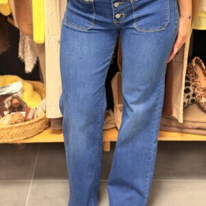 Pantalon jean bleu moyen effet used, coupe droite avec poches cargo appliquées à pressions sur les cuisses, style cargo chic, porté dans une boutique.