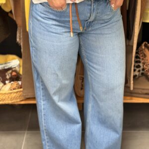 Pantalon jean bleu clair, coupe droite ample avec cordon orange à la taille, porté dans une boutique avec portants vêtements jaunes et paniers