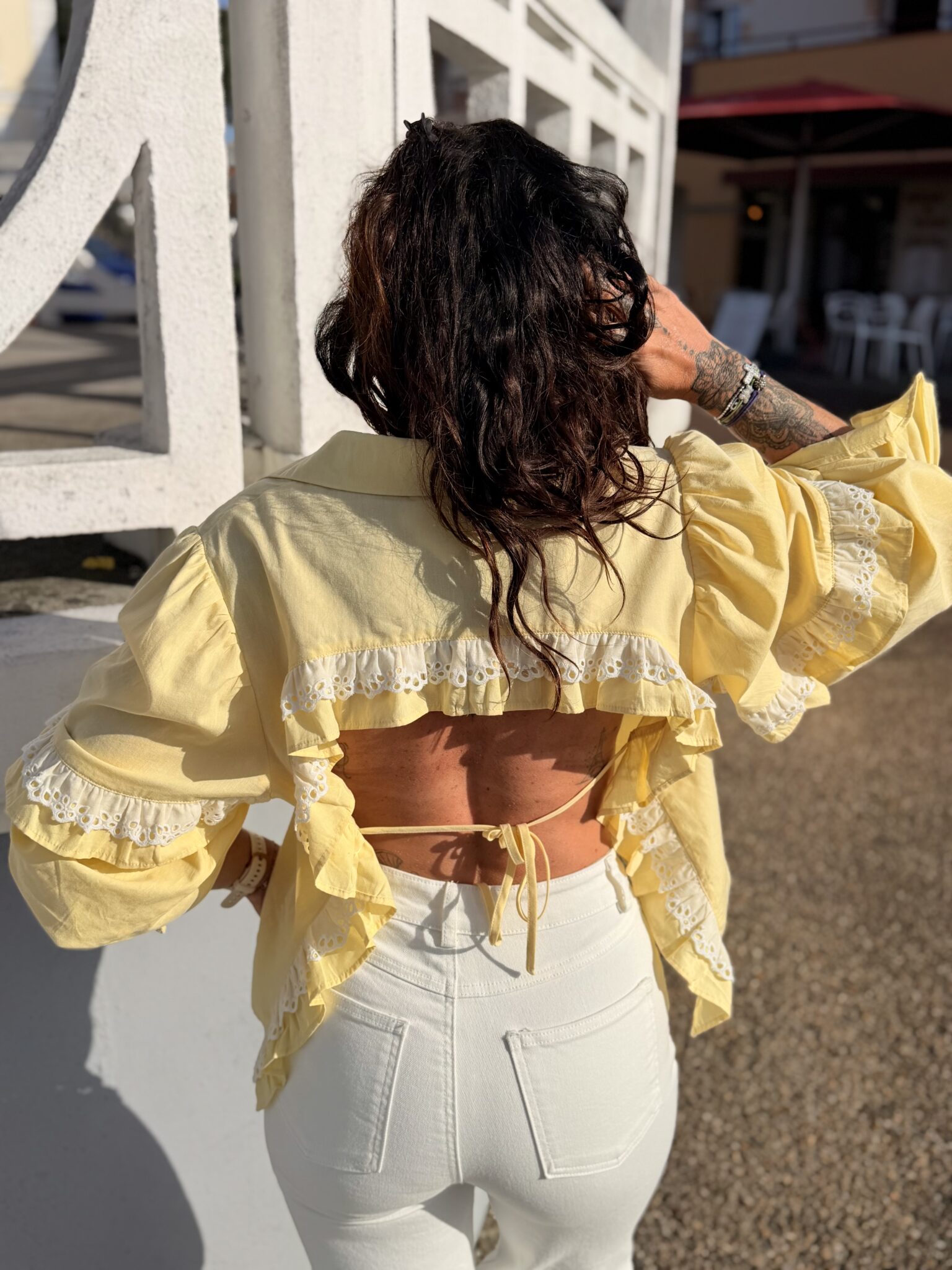 Femme aux cheveux brin mi long porte une chemise à volants et ouverte dans le dos avec un cordon très tendance et originale