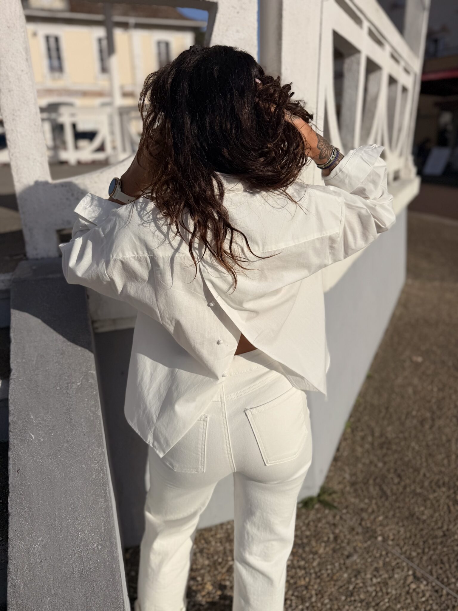 femme aux cheveux mi long brun portant une blouse blanche tendance et originale ouverte dans le dos avec des boutons