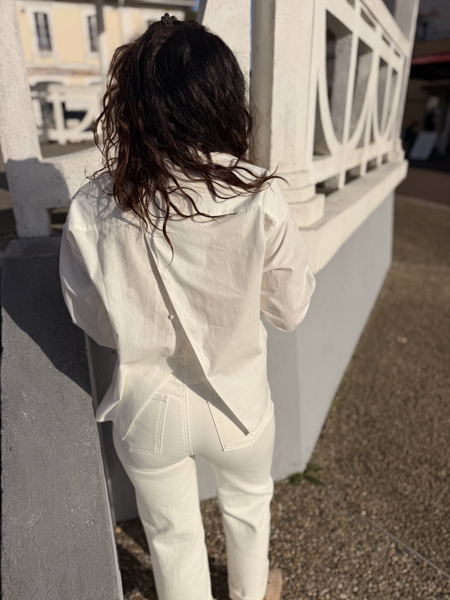 femme aux cheveux mi long brun portant une blouse blanche tendance et originale ouverte dans le dos avec des boutons