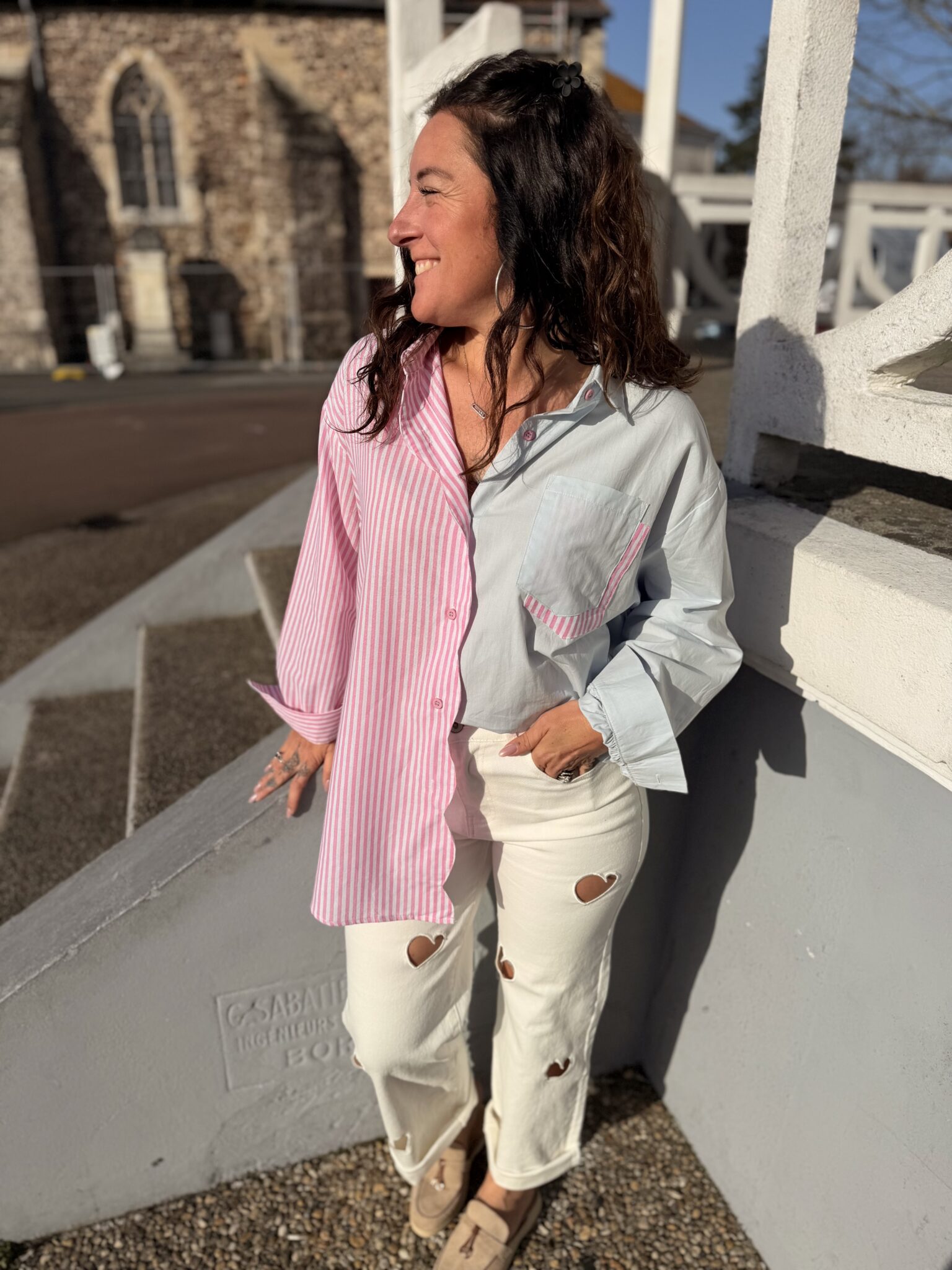 Femme aux cheveux brin mi long porte une chemise bi colore tendance rose et bleu, avec un peu de rayures
