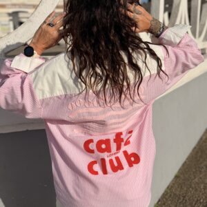 Femme aux cheveux brin mi long porte une chemise à rayures rose et blanche avec des broderies tendance café club
