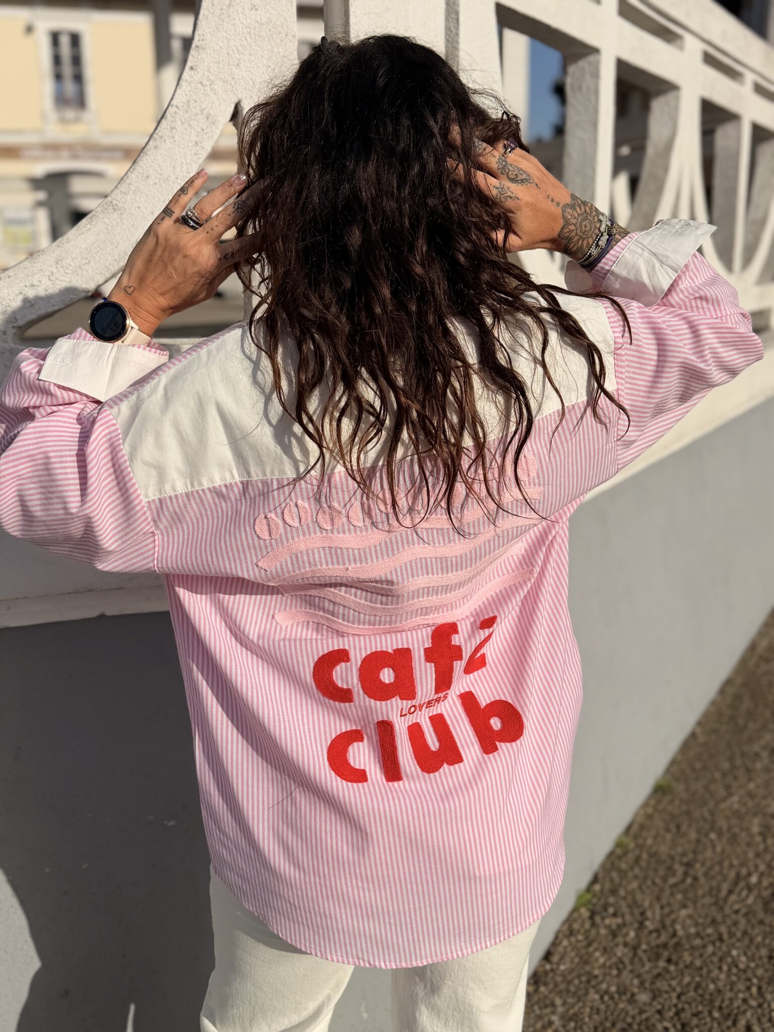 Femme aux cheveux brin mi long porte une chemise à rayures rose et blanche avec des broderies tendance café club