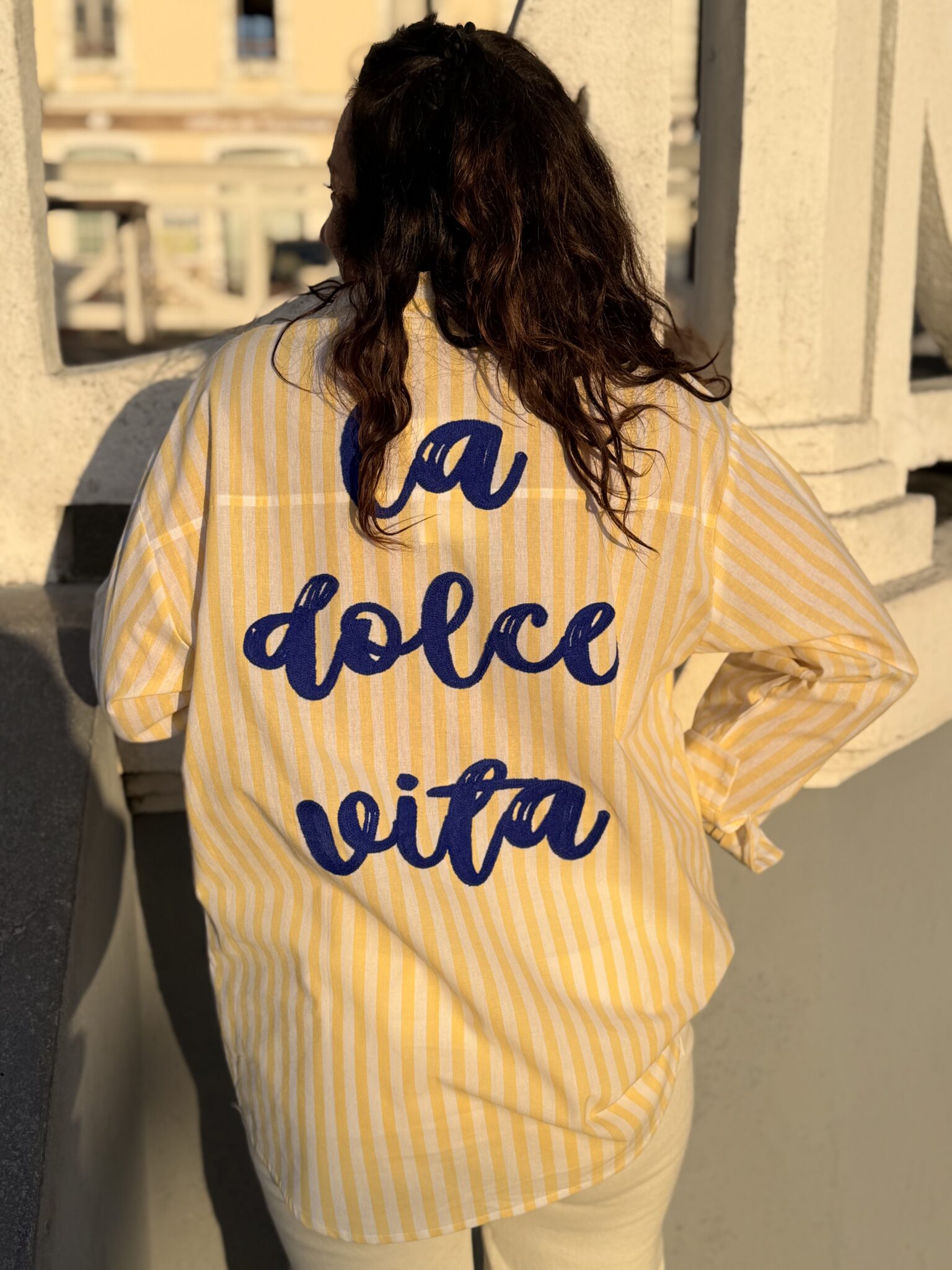 femme cheveux mi long brun porte une chemise à fines rayures avec une inscription dans le dos originale et tendance