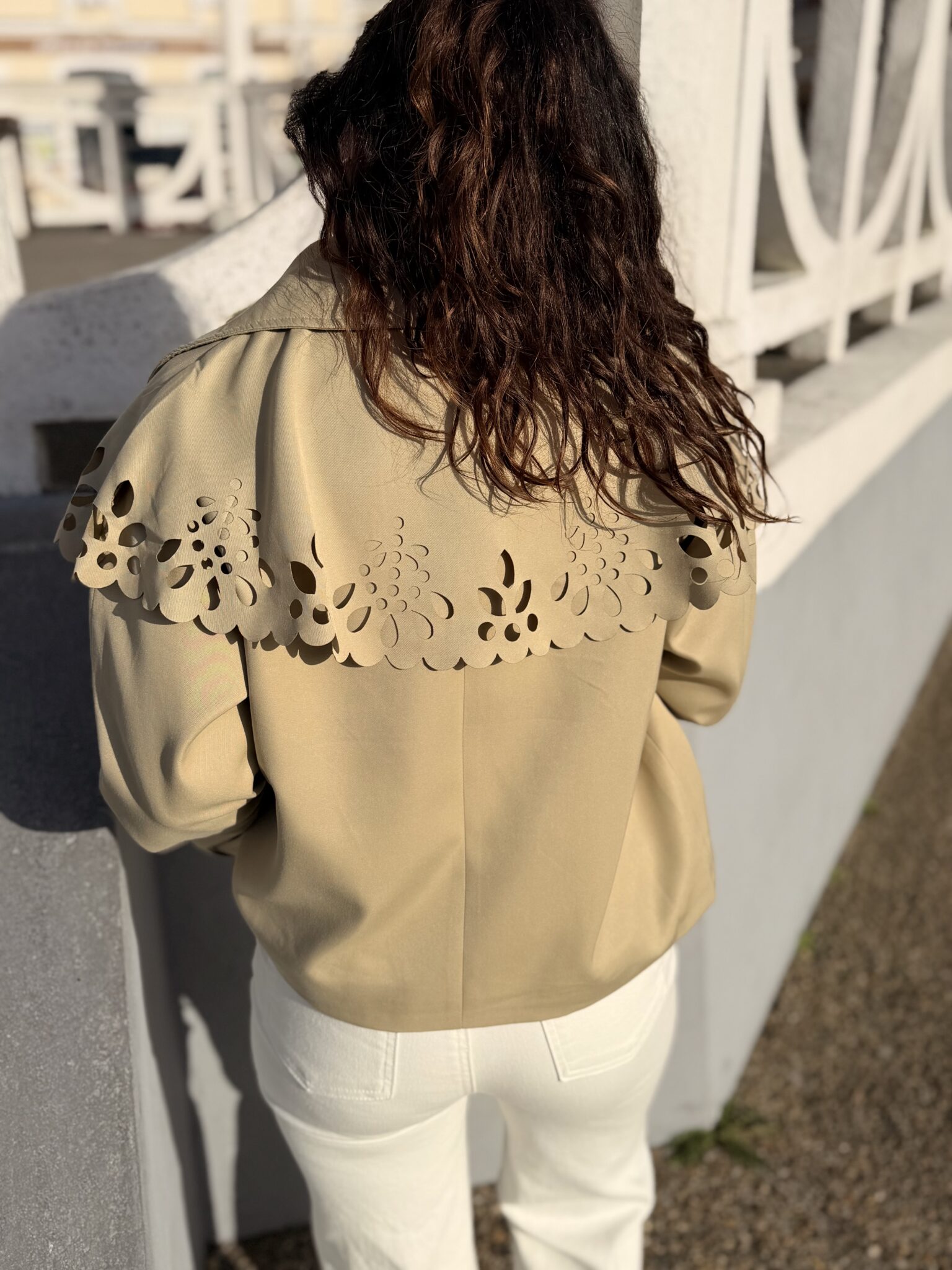 Femme aux cheveux brin mi long porte une veste beige avec une cape en dentelle originale et tendance