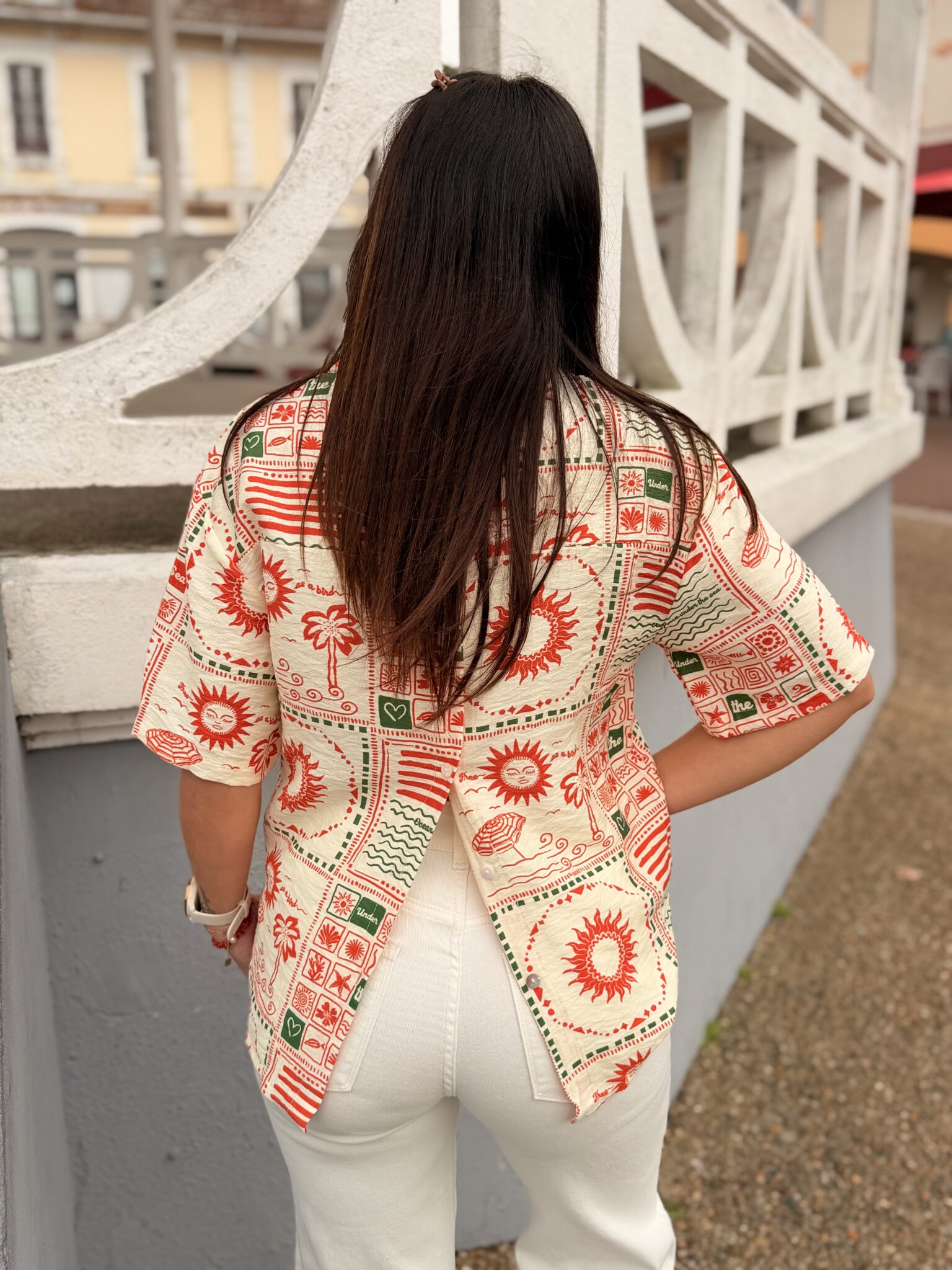 femme cheveux mi long brune porte chemise courte motif Summer soleil, palmiers, ouverte dans le dos