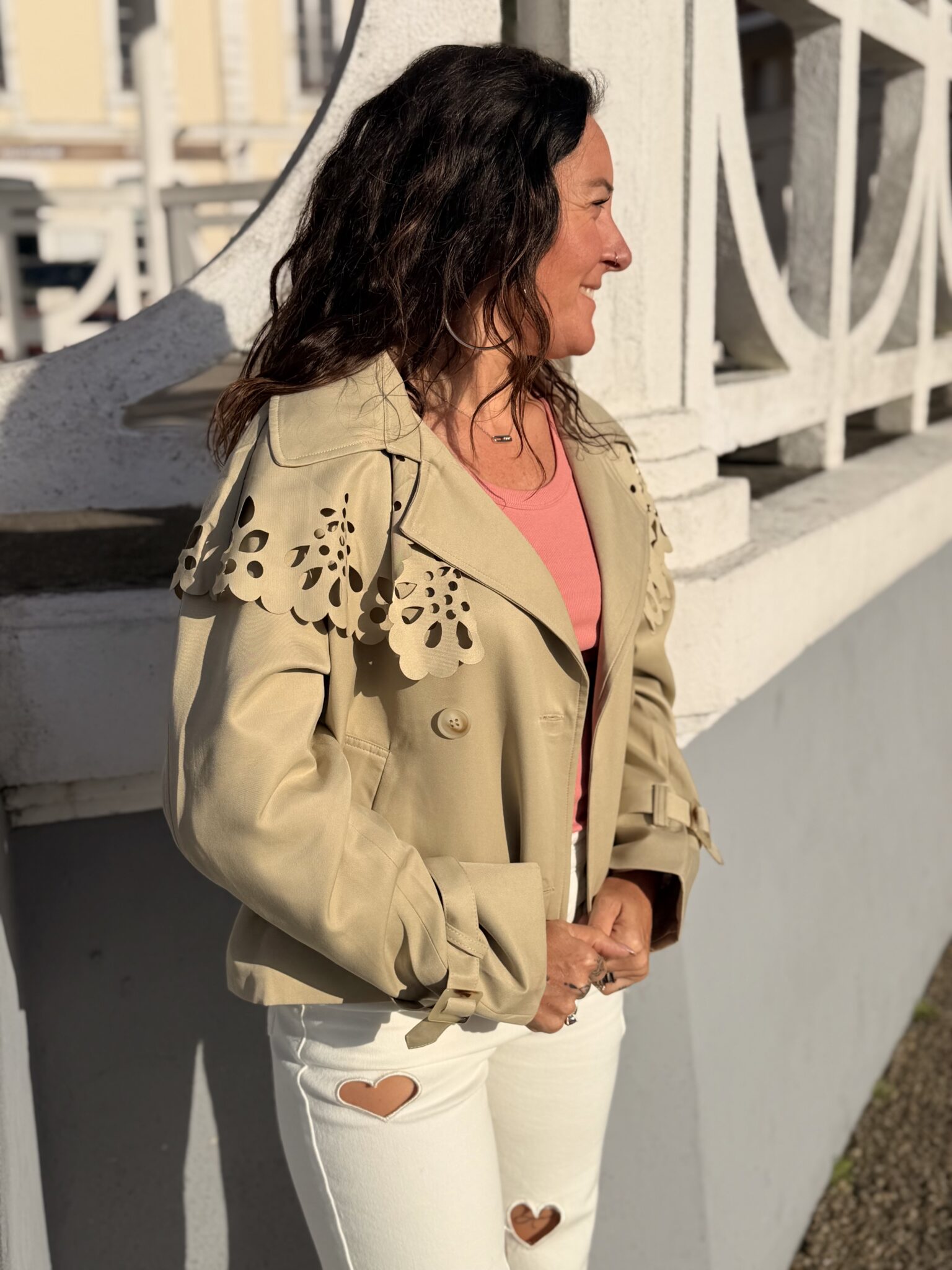 Femme aux cheveux brin mi long porte une veste beige avec une cape en dentelle originale et tendance