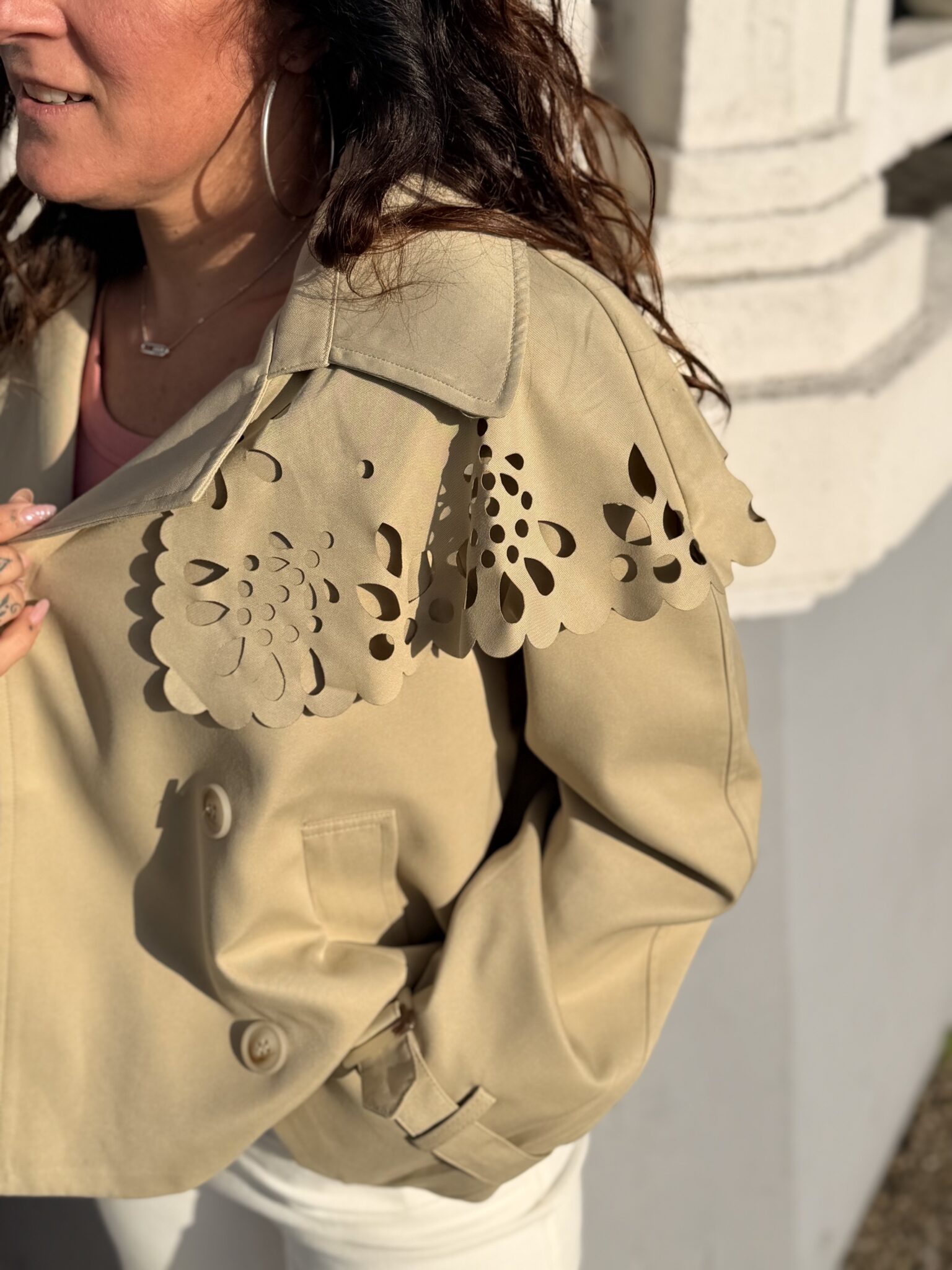 Femme aux cheveux brin mi long porte une veste beige avec une cape en dentelle originale et tendance