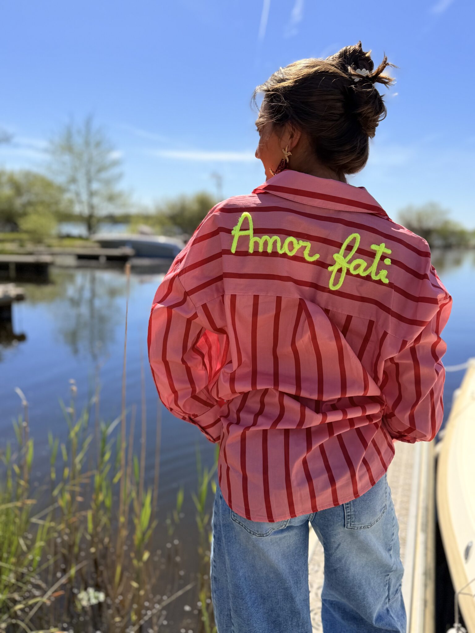 femme brune porte chemise rayé rose et rouge avec écriture dans le dos jaune fluo