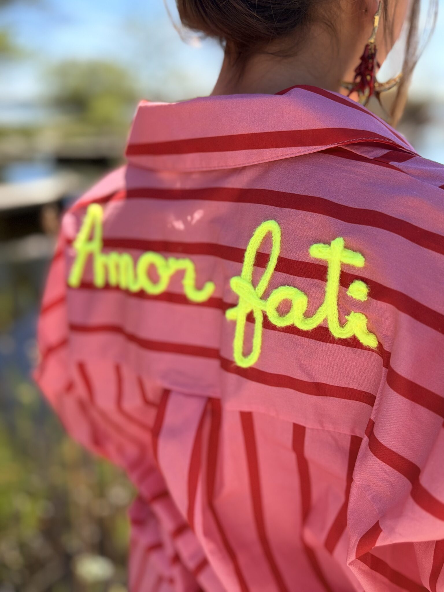 femme brune porte chemise rayé rose et rouge avec écriture dans le dos jaune fluo