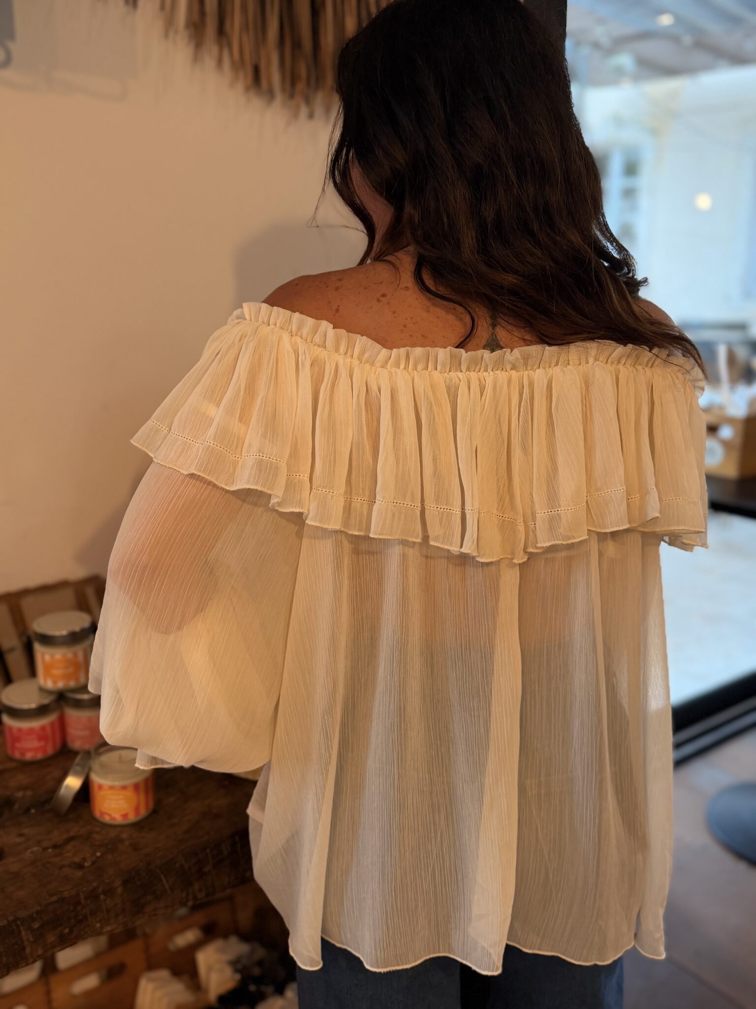 femme brune porte une blouse couleur crème style voilage épaules dénudées