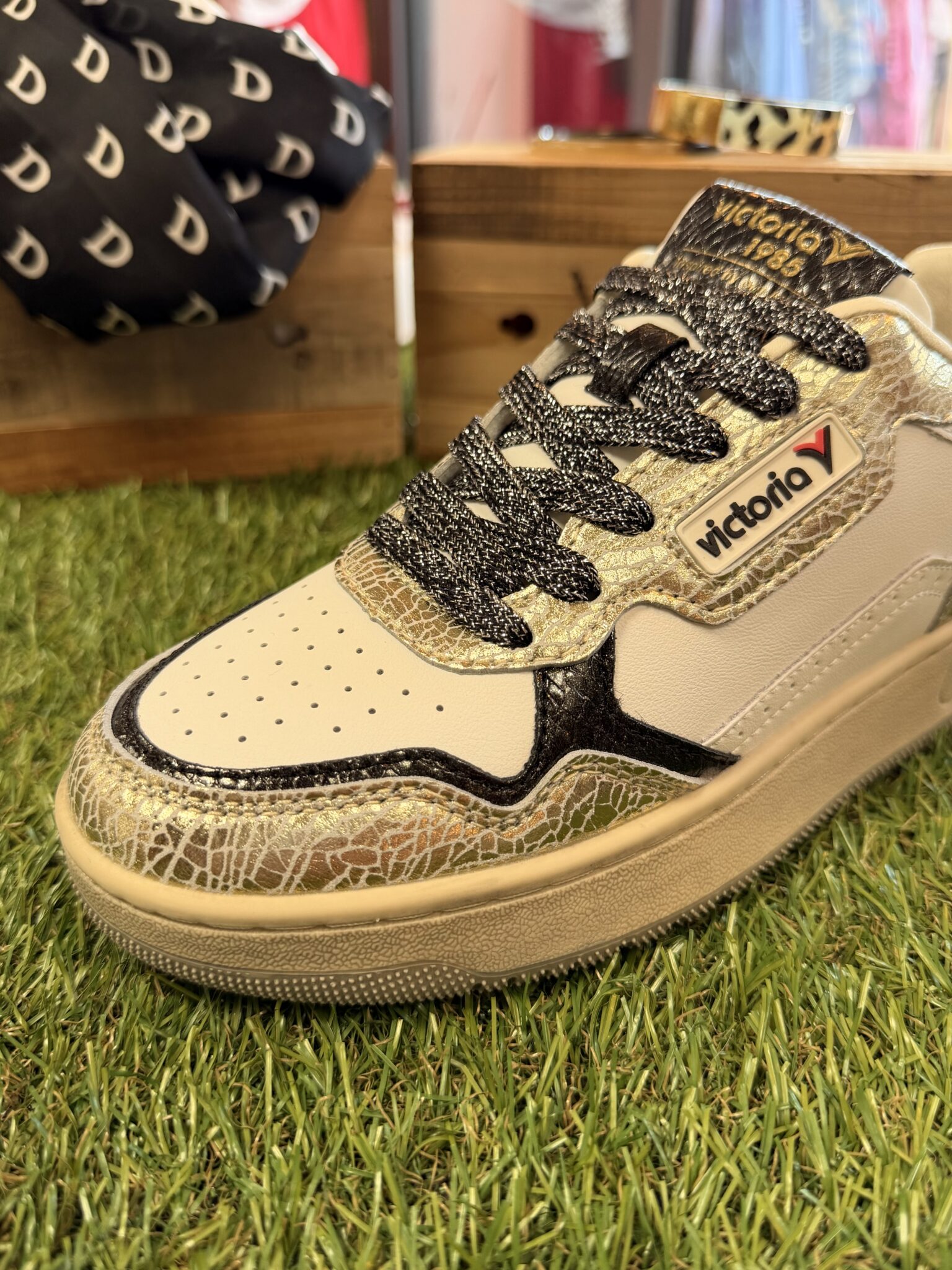 Basket Victoria pour femme dans des tons beige, doré et noir. Modèle bas avec empiècements métallisés texturés, lacets noirs, bout perforé et semelle épaisse d’inspiration rétro.